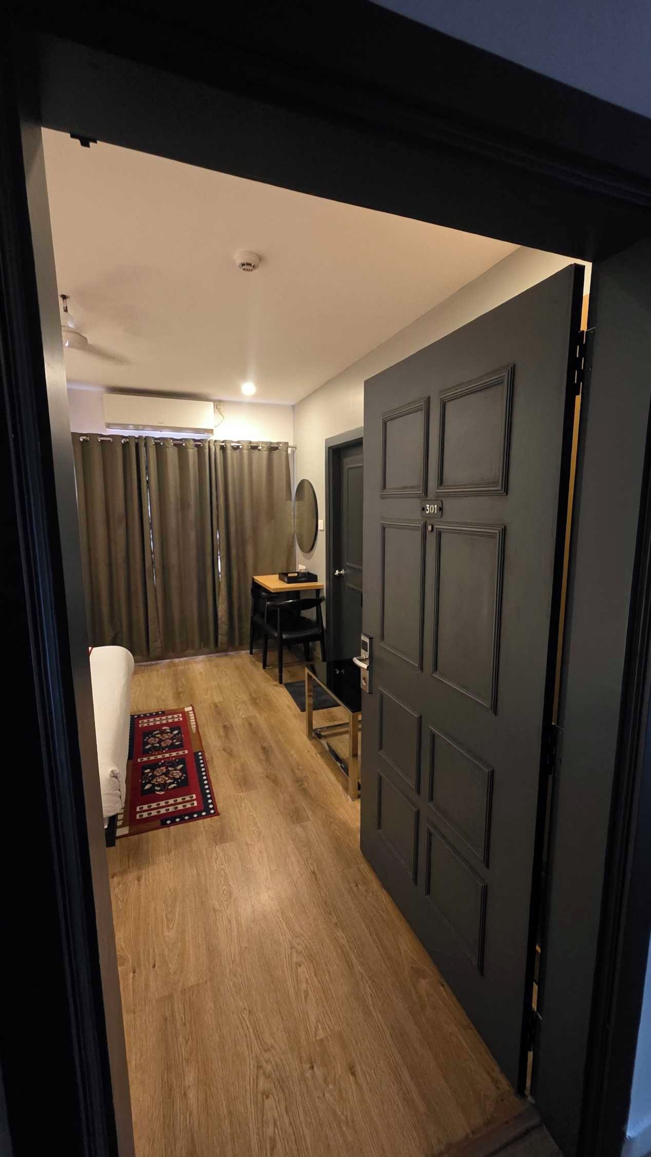 Un pasillo con suelo de madera, una puerta con un número y una pequeña mesa con una silla.