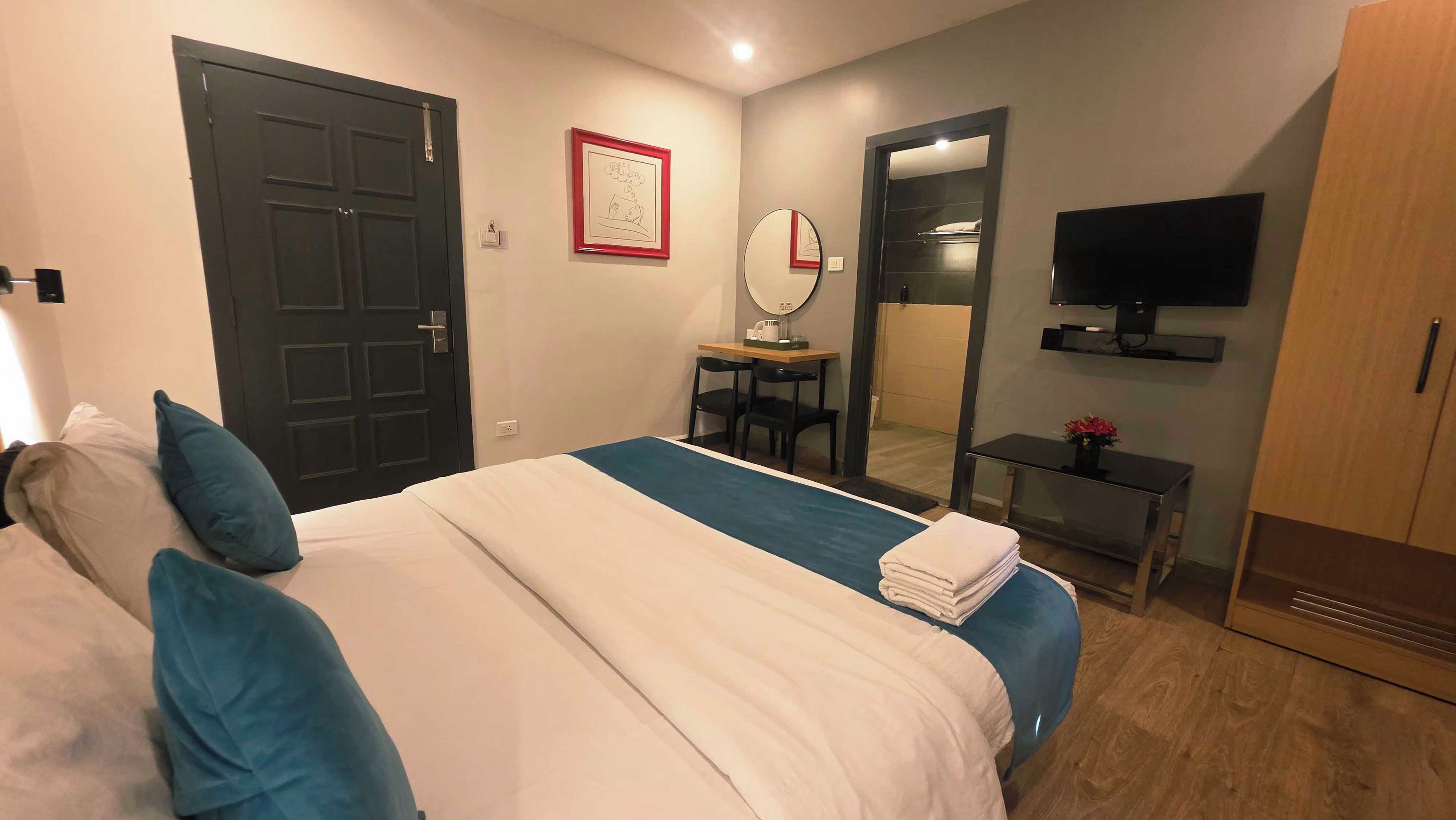A hotel room with a bed, a desk, a chair, a mirror, a television, and a wardrobe.