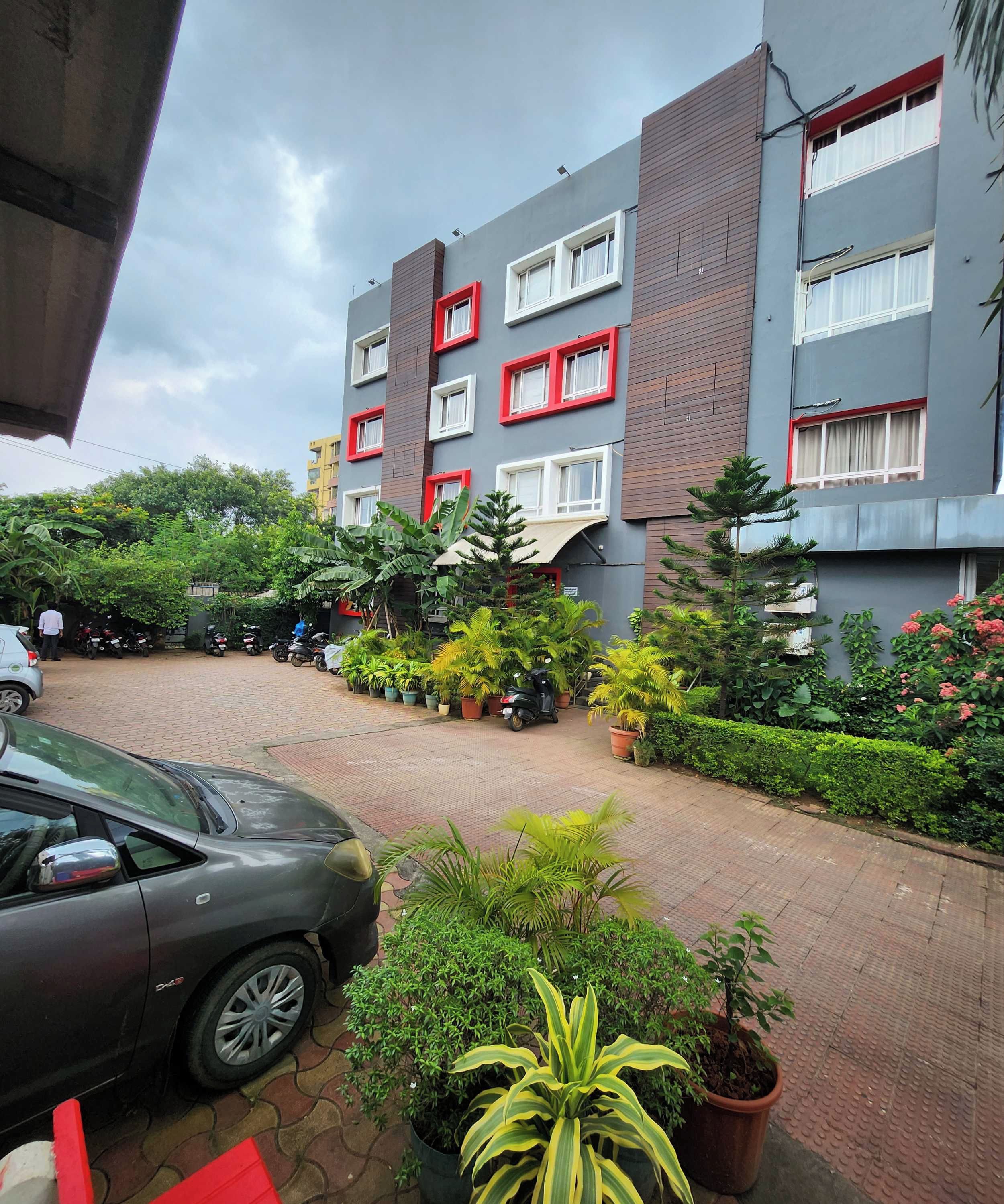 A multi-story residential building with balconies, a paved driveway, and potted plants.