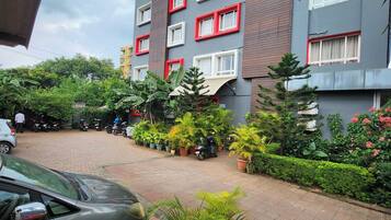 A multi-story residential building with balconies, a paved driveway, and potted plants.