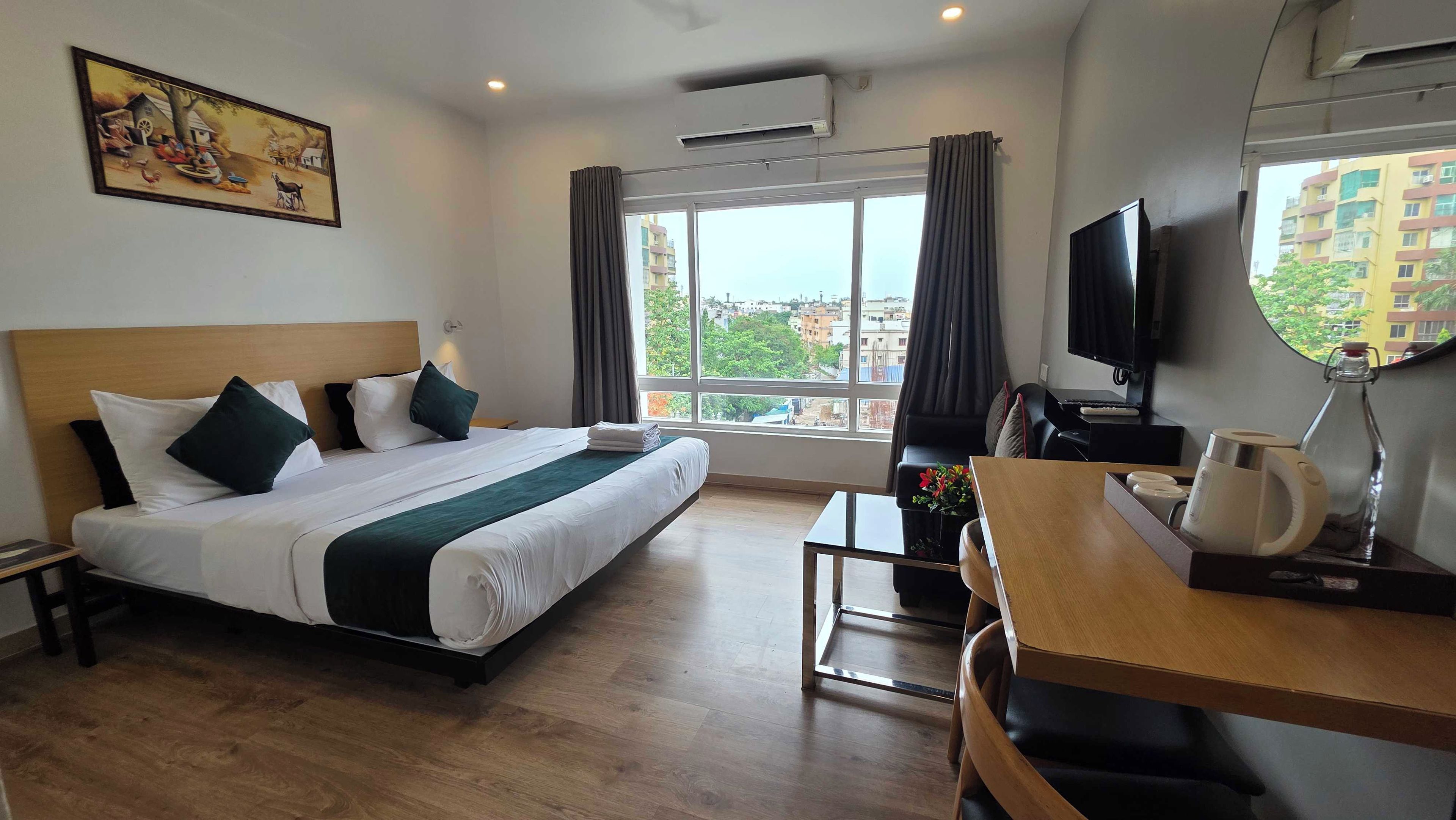 Habitación de hotel con una cama grande, un escritorio, un televisor y una ventana con vista a la ciudad.
