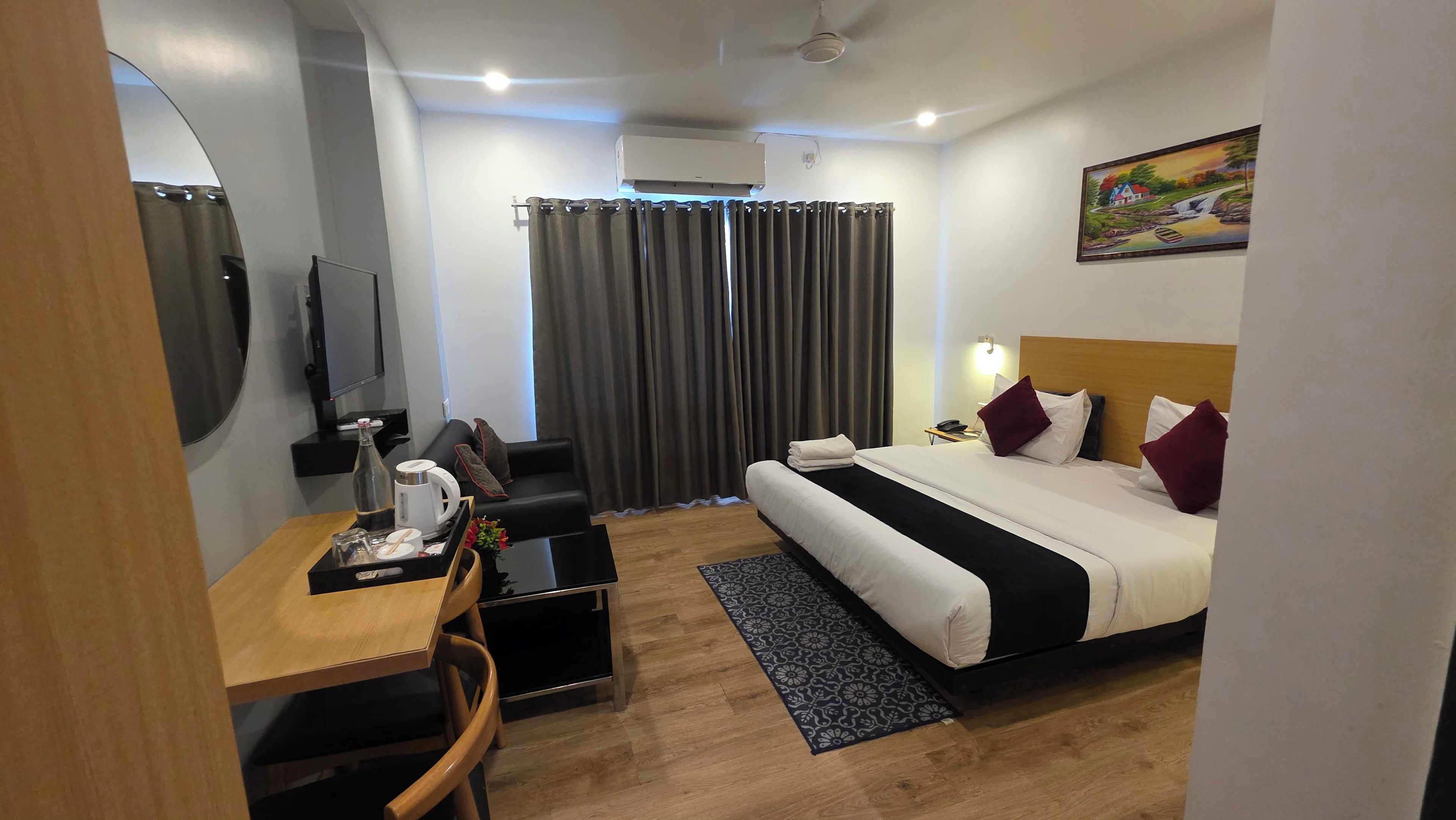 A hotel room with a bed, a desk with a chair, a television, and a painting on the wall.