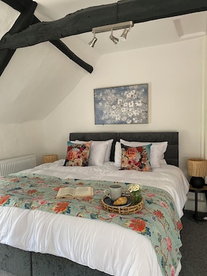 Ein Schlafzimmer mit einem großen Bett, floralem Bettzeug, einem Buch, einer Tasse und einem Korb mit Blumen.