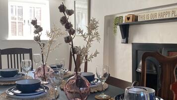 A dining table set with blue plates, silverware, and glassware, with a vase of dried flowers and a decorative wreath on the wall.