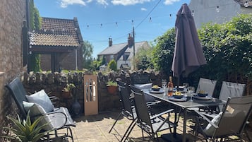 An outdoor patio with a table set for dining, surrounded by stone walls and potted plants.