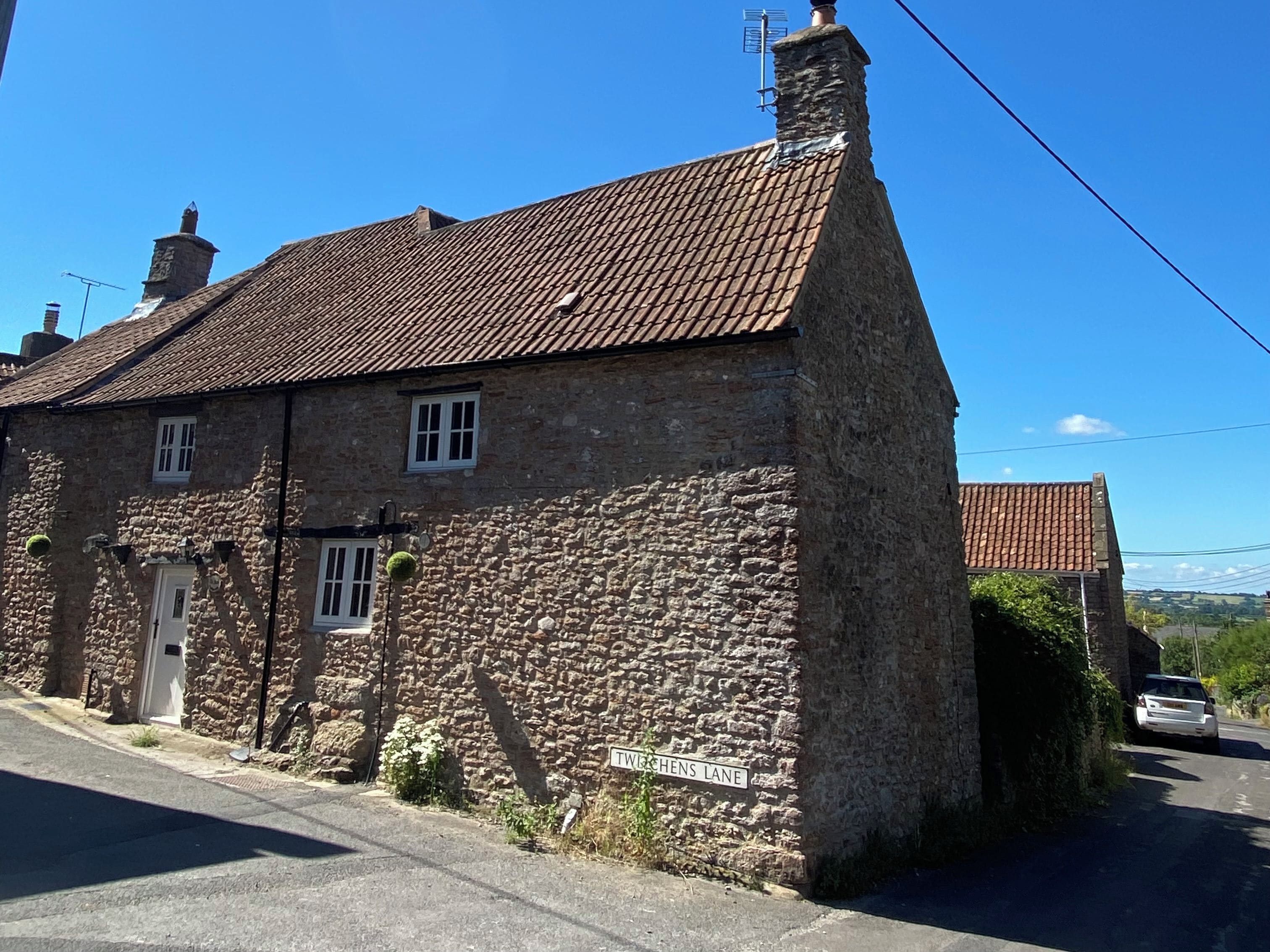 A stone building with a tiled roof, a visible chimney, and a street sign indicating 'TWECHENS LANE.'