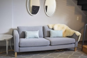 A grey sofa with two pillows, a small round table, and two wall-mounted mirrors. - Urban Living Home with Jacuzzi (Agios Onoufrios)