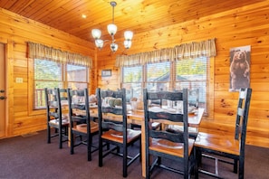 A wooden interior with a dining table and chairs, a chandelier, and windows with curtains. - Bear Cave | Theater, Arcade & Hot Tub | 3 King Suites | Sleeps 10 (Gatlinburg)