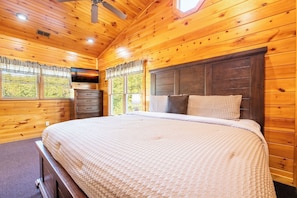 A wooden cabin bedroom with a bed, dresser, and a television on a wall. - Bear Cave | Theater, Arcade & Hot Tub | 3 King Suites | Sleeps 10 (Gatlinburg)