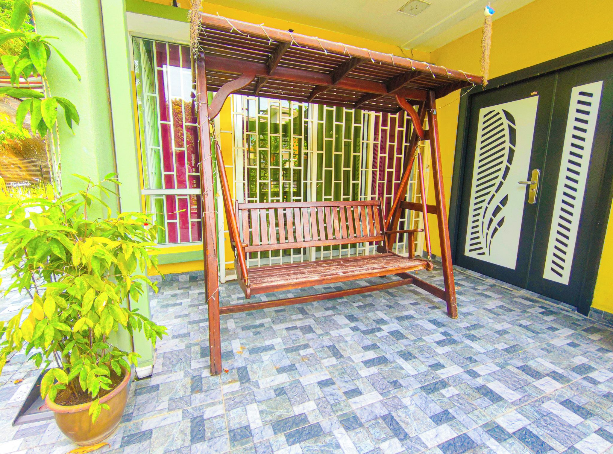 Un columpio de madera en una habitación con baldosas de diseño y una planta en maceta.