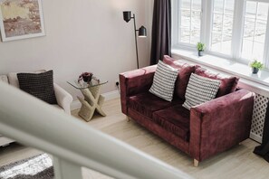 Ein modernes Wohnzimmer mit einem roten Samtsofa, einem Glastisch und einem minimalistischen Einrichtungsstil.