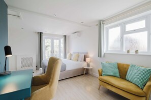 Ein Hotelzimmer mit einem Bett, einer Couch, einem Schreibtisch mit Lampe und einem fenster mit Vorhängen.