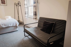 A room with a bed, a sofa, a radiator, and a window with curtains. - Comfortable 3 Bedroom Townhouse Sleeps 6 (Northampton)