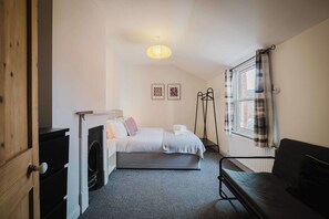 A compact bedroom with a bed, a radiator, a window with curtains, and a hanging light fixture. - Comfortable 3 Bedroom Townhouse Sleeps 6 (Northampton)