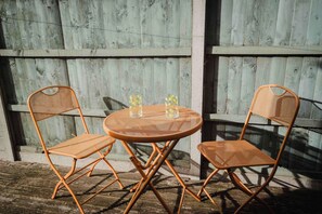 A round outdoor table with two wicker chairs, set against a wooden wall. - Comfortable 3 Bedroom Townhouse Sleeps 6 (Northampton)