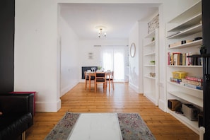 A living room with a black sofa, a coffee table, and a bookshelf filled with books and games. - Comfortable 3 Bedroom Townhouse Sleeps 6 (Northampton)