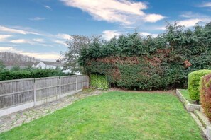 Ein Garten mit Holzzaun, Rasenfläche und dichter Hecke.