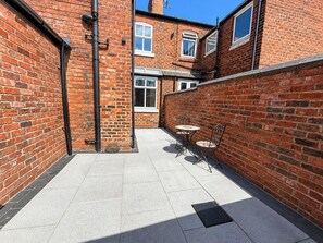 A courtyard with a brick wall, a tiled floor, and a small table with chairs. - The Urban Nest – Stylish Hoole Stay for 4 (Cheshire West and Chester)