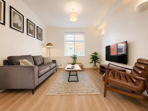 Een woonkamer met een bank, een salontafel, een televisie en een leren fauteuil.