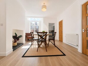 A modern interior with a dining area featuring a round table and chairs, a potted plant, and a view to the outside. - The Urban Nest – Stylish Hoole Stay for 4 (Cheshire West and Chester)
