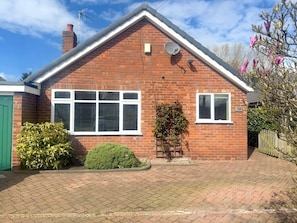 A brick house with a pitched roof, a satellite dish, and a green door. - Greenfields Apartment (Christleton)