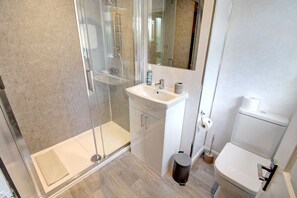 A modern bathroom with a glass-enclosed shower, a white sink, and a toilet. - Greenfields Apartment (Christleton)