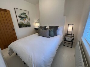 Ein Schlafzimmer mit einem Bett, Kissen, einem Nachttisch mit Lampe, einer Heizung und einem Fenster.