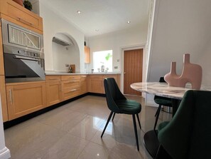 Eine moderne Küche mit Holzschränken, einem Einbauofen und einem Essbereich mit rundem Tisch und Stühlen.