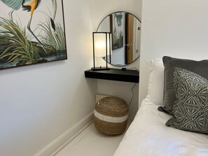 Une chambre à coucher comprenant un lit, une table de chevet, un miroir, une étagère fixée au mur et un petit pouf rond.