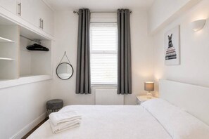 Ett sovrum med en säng, ett sängbord med en lampa, en upphängd spegel, ett element och en garderob.