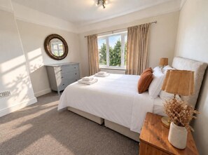 A bedroom with a bed, a bedside table with a lamp, a dresser, and a window with curtains. - The Family Holiday in Chester, Parking and Garden (Cheshire West and Chester)