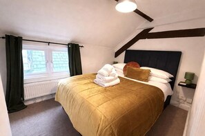 Een hotelkamer met een bed, een raam met gordijnen, een radiator, een nachtkastje met een lamp en een hoofdbord.