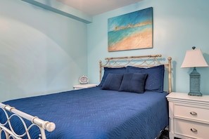 A bedroom with a bed, a nightstand, a lamp, a painting, and a clock. - Victory Hull  - Bayfront Condo in the Heart of Stone Harbor, NJ (Stone Harbor)