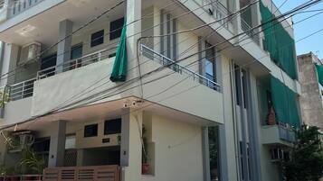 A multi-story residential building with balconies, a gated entrance, and a parked car and motorcycle.