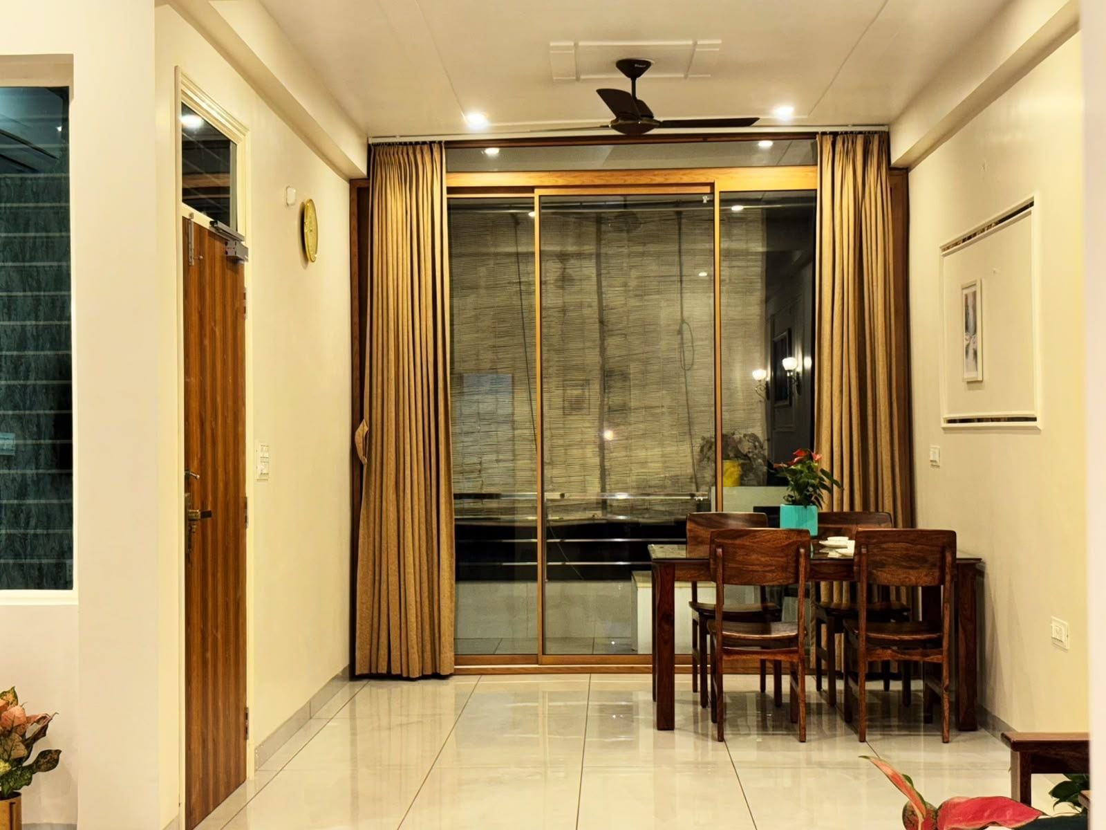 A dining area with a glass partition, wooden chairs, a table, and a ceiling fan.