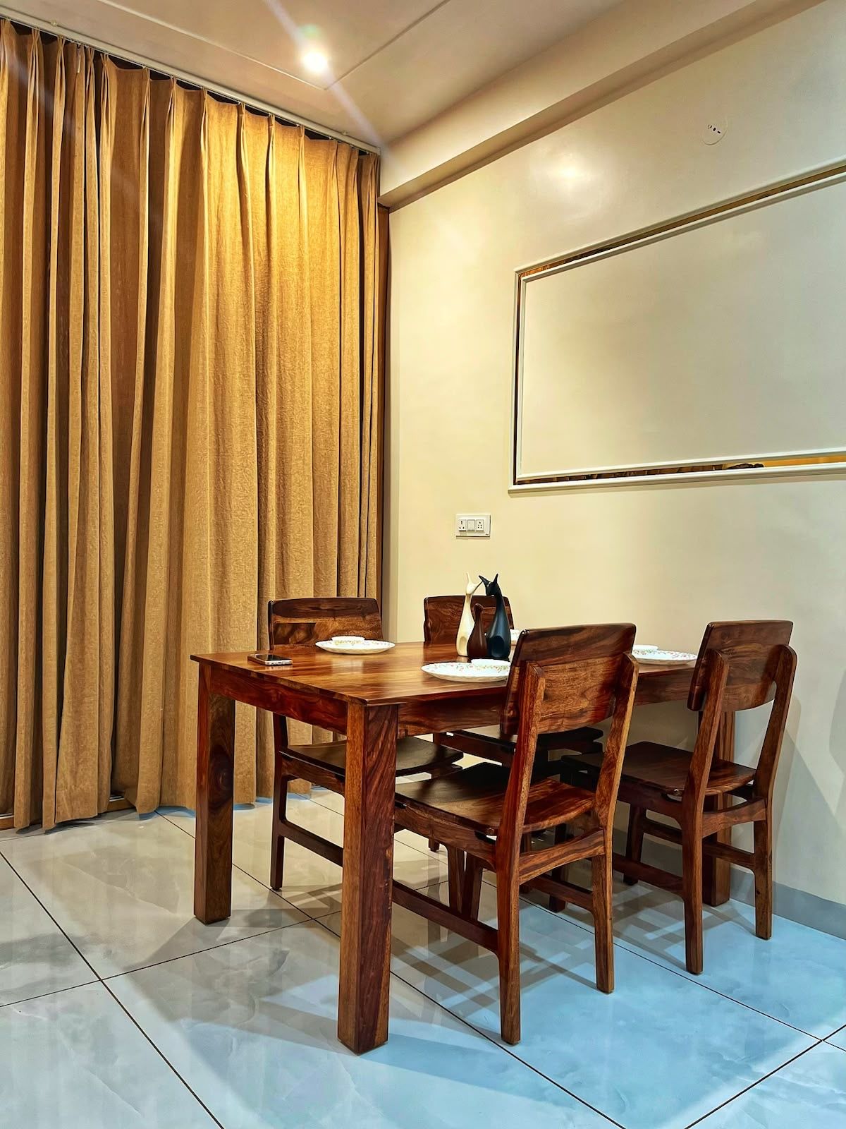 Uma sala de jantar com mesa e cadeiras de madeira, uma janela grande com cortinas e uma televisão de tela plana fixada na parede.