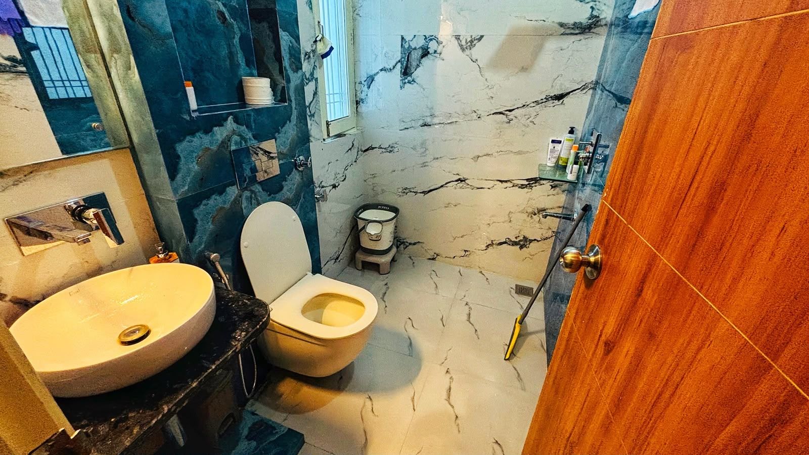 A bathroom with a marble floor, a toilet, a sink, and a wooden door.