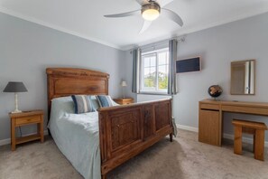 A bedroom with a wooden bed, bedside tables, a desk, a chair, a ceiling fan, a window with curtains, and a flat-screen TV. - Barbridge Canal Holiday (Cheshire East)