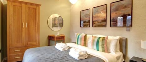 A bedroom with a large bed, a wooden wardrobe, a round mirror, and three landscape paintings on the wall.