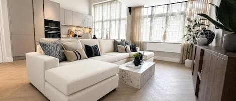 A modern living room with a sectional sofa, a coffee table, and a kitchen in the background.