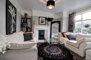 A living room with a fireplace, two sofas, a coffee table, and a bookshelf. - The Botanical Holiday by Cheshire Escapes (Cheshire West and Chester)