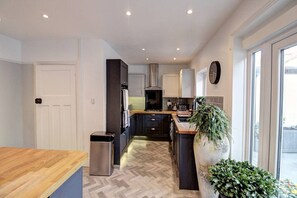 A modern kitchen with a herringbone floor pattern, stainless steel appliances, and a large window providing natural light. - The Botanical Holiday by Cheshire Escapes (Cheshire West and Chester)