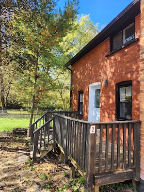 A brick building with a wooden deck and a number '2' sign. - Lovely renovated one bedroom getaway (Meaford)