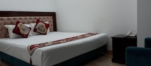 A hotel room with a bed, a bedside table with a phone, and a chair. - Hotel D Palace (Dhaka)