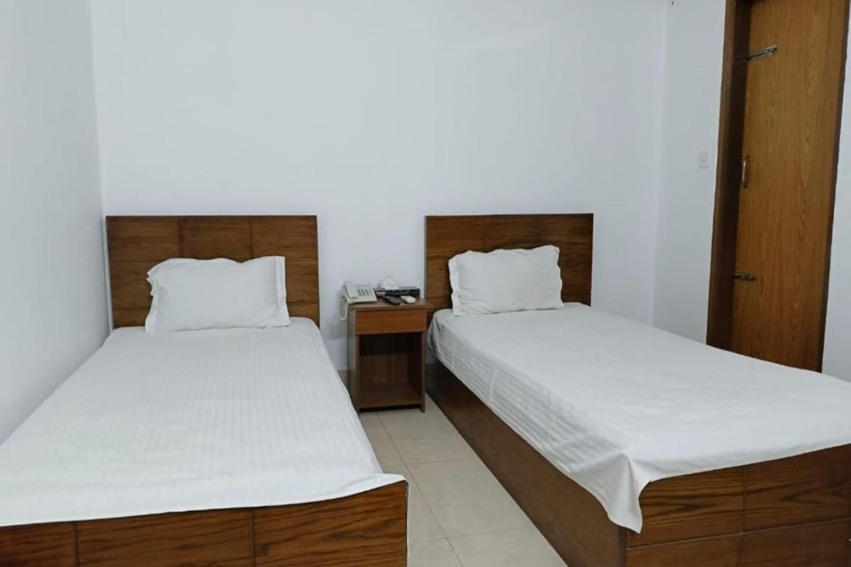 A room with two single beds, wooden headboards, white bedding, a wooden nightstand with a telephone, and a wooden door.