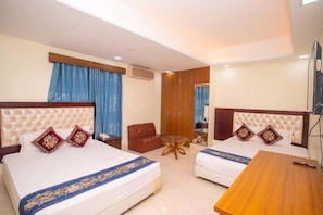 A hotel room with two beds, a sofa, a small round table, and a TV. - Hotel D Palace (Dhaka)
