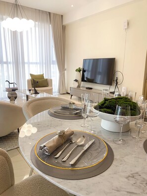 Et moderne spiseområde med et marmorbord dækket til fire personer, et fjernsyn og en dekorativ mos-installation.