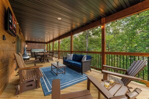 A covered outdoor deck with seating, a grill, and a TV screen. - 3BD 3BA Cabin Private Hot Tub Indoor/Outdoor Pools Lazy River! (Hollister)
