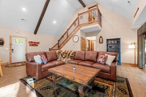 Un vaste salon doté d’un canapé d’angle en cuir marron, d’une table basse en bois et d’un escalier menant à l’étage supérieur.