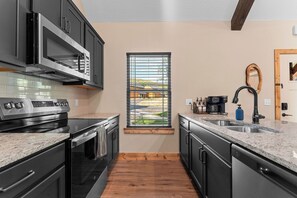 A modern kitchen with stainless steel appliances, a window with blinds, and a coffee maker. - 3BD 3BA Cabin Private Hot Tub Indoor/Outdoor Pools Lazy River! (Hollister)